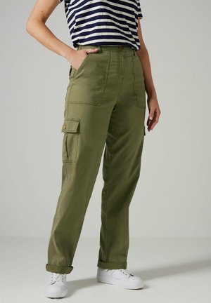Pantalons cargo vert olive avec une coupe décontractée, dotés de poches latérales, de bas de pantalon retroussés et d'un tissu texturé. Associés à un haut rayé et des baskets blanches.