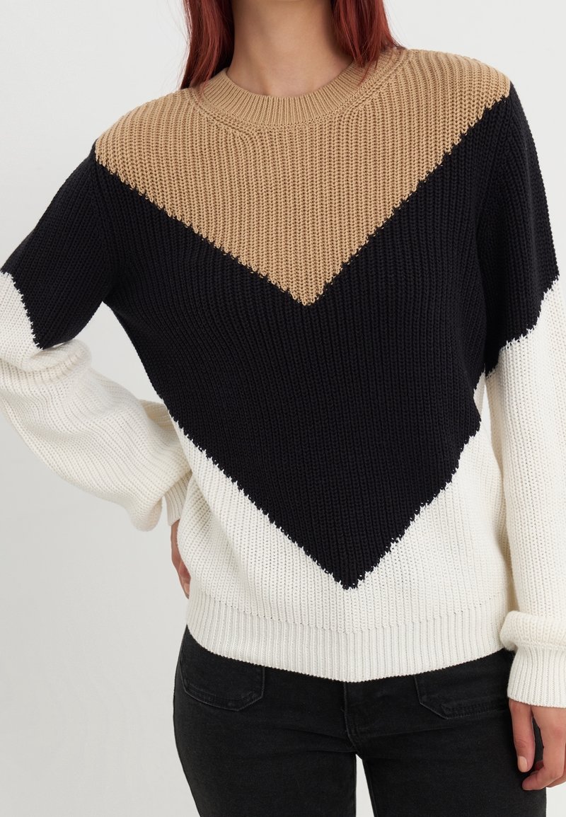 Dzianinowy sweter z blokowym wzorem w beżowym, czarnym i białym kolorze. Teksturowana tkanina, okrągły dekolt i ściągacze na mankietach.
