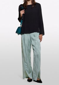 Svart långärmad topp, ljusgröna vida byxor med ett subtilt mönster och sidöppningar, kompletterad med en tealväska och svarta lägenheter.