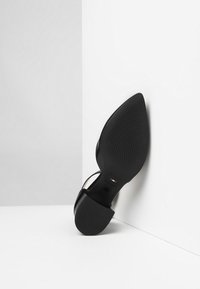 Scarpa nera con tacco alto e punta affusolata, suola in gomma e soletta testurizzata. Presenta sottili cinture alla caviglia e un dettaglio di branding italiano.