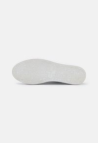 Biała podeszwa trampka z teksturowanym kauczukowym bieżnikiem i logo. Gładka powierzchnia, okrągły kształt i minimalistyczny design bez sznurowadeł ani dodatkowych elementów.