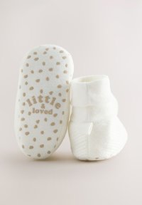 Chaussons en tissu blanc à texture douce, avec une semelle beige tachetée et le texte "little & loved" imprimé en dessous.