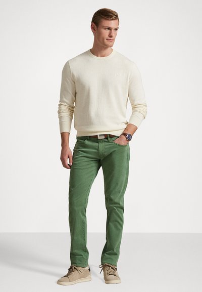 Beige gebreid sweater, groene slim-fit chinos en beige sneakers. De outfit heeft een casual ontwerp met minimale accenten en texturen.