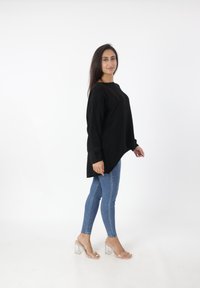 Zwarte oversized gebreide trui met een ronde halslijn, gecombineerd met blauwe skinny jeans en doorzichtige block-heeled sandalen. Eenvoudige, casual look.