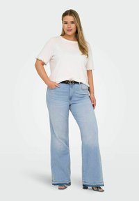 Lichtroze top met korte mouwen en kantafwerking, gecombineerd met lichtblauwe flare jeans met hoge taille en ruwe zoom, accessorized met een zwarte riem.