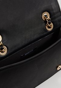 Black leather handbag with a smooth texture, featuring gold circular hardware and a black chain detail. Interior label visible.