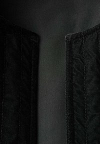 Tela negra, con una textura suave en el centro y detalles laterales de un acabado tipo denim. Costuras visibles a lo largo de los bordes, diseño minimalista.
