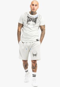 Heledhall hall katab T-shirt TAPOUT, millel on sinine ja must graafika ning tiiva disain, koos sobivate lühikestega, millel on logo aktsendid ja taskud.