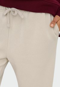 Helle beige Jogginghose mit elastischem Bund, Kordelzugdetails und Seitentaschen, aus einem weichen, strukturierten Stoff.