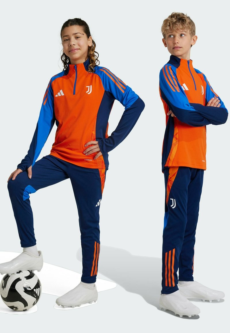 Set für Jugendsportbekleidung mit einem orangefarbenen Zip-up-Oberteil mit blauen Akzenten und passenden marineblauen Hosen, verziert mit weißen Logos und orangefarbenen Streifen.