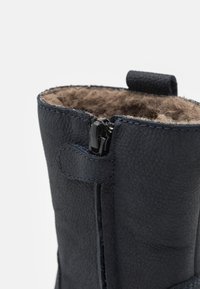 Botte en cuir bleu marine avec fermeture éclair, doublure textile douce et couture contrastante le long des bords. Surface texturée et design robuste.
