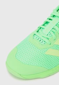 Scarpa da atletica verde con tomaia in rete, superficie testurizzata e suola in gomma liscia. Ha lacci piatti e logo sulla linguetta.