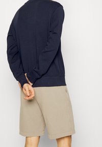 Námořnická modrá mikina s dlouhými rukávy, žebrované manžety a lem, spárovaná s světle béžovými šortkami s ohrnutými nohavicemi a bočními kapsami.