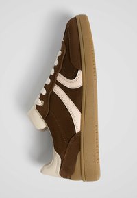 Baskets en daim marron avec un embout en cuir beige, des lacets crème et des accents roses. Elles présentent une semelle extérieure en gomme texturée et une forme arrondie.