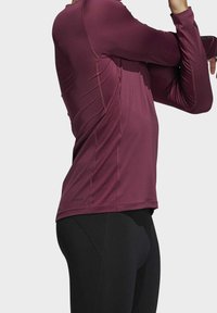 Bordowy, długi rękaw sportowy top z dopasowanym krojem, płaskimi szwami i materiałem odprowadzającym wilgoć, w połączeniu z czarnymi legginsami.