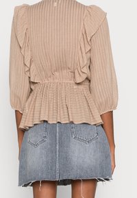 Beige, tekstureret top med voluminøse ærmer og peplum-detalje, kombineret med en grå denimnederdel med fransede kanter og baglommer.