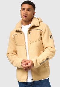 Chaleco de forro polar beige con cremallera en la parte delantera, capucha y tejido texturizado. Cuenta con un panel liso en el pecho y un bolsillo con cremallera en la manga.