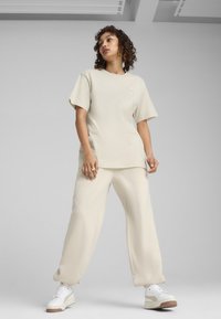 Beżowy bawełniany t-shirt z krótkimi rękawami i okrągłym dekoltem, zestawiony z beżowymi spodniami o szerokich nogawkach oraz białymi trampkami, z subtelnym logo.