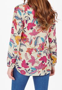 Blusa a maniche lunghe color crema con un vivace motivo floreale in rosa, giallo e blu. Presenta un orlo arrotondato e una morbida texture del tessuto.