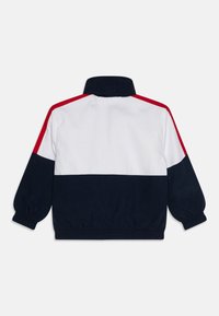 Farbblockierte Jacke mit navyblauen, weißen und roten Panels, ausgestattet mit einem hohen Kragen und elastischen Bündchen für einen sicheren Sitz.