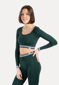 Zielony krótki top z długim rękawem, dekoltem w kształcie łódki i białym paskiem przy krawędzi, zestawiony z dopasowanymi wysokim stanem legginsami z podobnymi paskami.