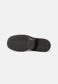 Black rubber shoe sole with textured grip pattern, featuring deep treads for traction and a smooth finish around the edges.