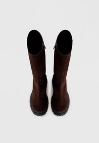 Par črne visoke zamazane čevlje iz temno rjave skuldne z obrobami in stranskimi zadrgami, prikazane z vrha na belem ozadju.