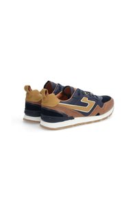 Baskets de sport en cuir et daim bleu marine, marron et beige. Semelle intermédiaire blanche et semelle extérieure en caoutchouc texturé. Avec tirant à l'arrière.