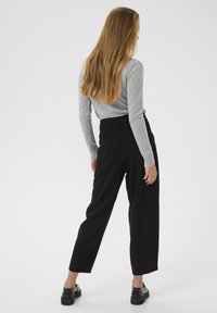 Gray long-sleeve top paired with high-waisted black trousers. Trousers have a tailored fit and tapered legs. Black shoes with a chunky sole.