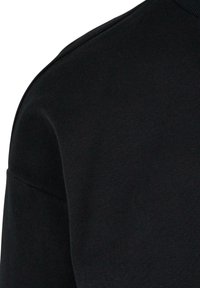 Pull-over noir à col rond, avec une texture lisse et une silhouette ajustée. Détail de couture visible le long de la couture de l'épaule.
