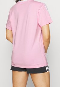 Rosa bomullströja med korta ärmar, rund halsringning och vita ränder längs axlarna. Designen är enkel och avslappnad.