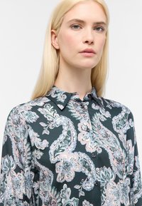 Blusa di seta verde scuro con un motivo paisley che presenta dettagli in rosa, blu e bianco. Tessuto finemente texture con colletto a bottoni.