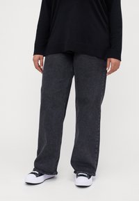 Black long-sleeve top paired with gray wide-leg jeans. The jeans have a smooth texture and subtle stitching detail. Footwear features black and white design.