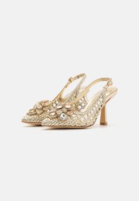 Tacchi slingback dorati con texture intrecciata, punta affusolata e decorazione floreale con gemme. Tacco sottile e cinturino regolabile.