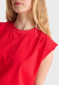 Top senza maniche in cotone rosso con collo rotondo e dettagli di cucitura discreti, caratterizzato da una texture morbida e una vestibilità comoda.