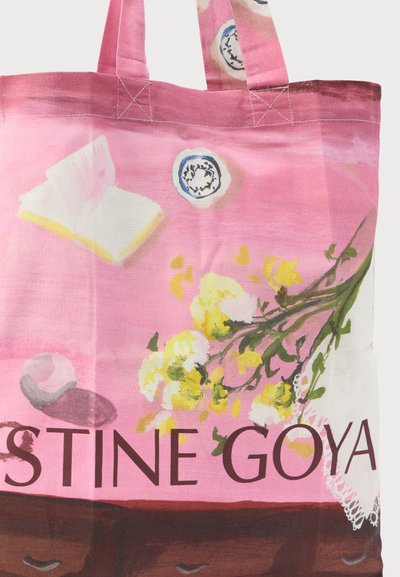 Ροζ τσάντα ώμου με κίτρινα λουλούδια, ένα ανοιχτό βιβλίο, ένα φλιτζάνι τσάι και το κείμενο "STINE GOYA" στο κάτω μέρος της τσάντας.