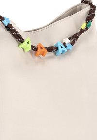 Cremefarbene Ledertasche mit einem braunen, geflochtenen Riemen. Der Riemen ist mit bunten Perlen in Form von Buchstaben in Blau, Orange, Grün und Weiß verziert.