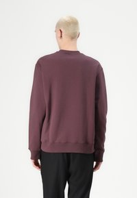Felpa color bordeaux con scollo a girocollo a costine, maniche lunghe e vestibilità morbida. Texture liscia e colore uniforme senza motivi o dettagli.