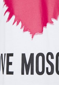 Bílý tričko s designem růžové skvrny na vrchní části a tučným černým textem "MILUJ MOSKVU" na spodní části. Bavlněný materiál.