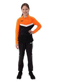 Completo sportivo JAKO con top arancione a maniche lunghe caratterizzato da dettagli bianchi e pantaloni neri, che mette in mostra un design sportivo e un tessuto testurizzato.