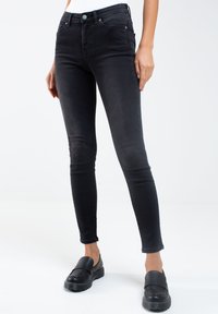 Jeans ajustados negros hechos de mezclilla con una textura suave, que presentan un diseño clásico de cinco bolsillos y una cintura de altura media para un ajuste ceñido.