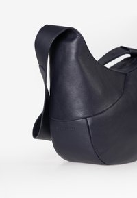 Borsa in pelle blu navy con una finitura liscia, design morbido e una sola tracolla. Presenta un discrete dettaglio del logo in rilievo.