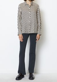 Camicia abbottonata in crema e navy con motivo geometrico, maniche lunghe, abbinata a pantaloni scuri aderenti e mocassini neri.