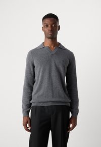 Gray v-neck sweater made of soft material, featuring a pointed collar and ribbed cuffs. Paired with black tailored trousers.