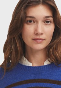 Blauer Strickpullover mit horizontalen braunen Streifen. Weicher Stoff und Rundhalsausschnitt mit einem kontrastierenden weißen Innenkragen.
