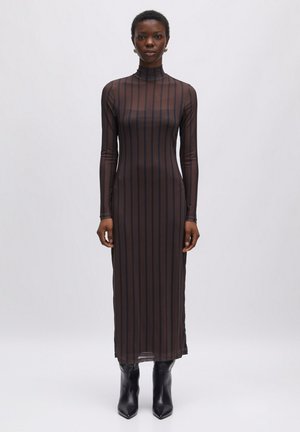 Durchsichtiges, langärmeliges, schwarzes Kleid mit vertikalen braunen Streifen, mit hohem Kragen und figurbetontem Schnitt, kombiniert mit schwarzen Knöchelstiefeln.