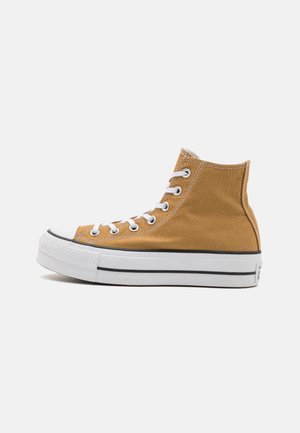 High-top lærredssneaker i brun med hvid gummisål, hvide snørebånd og sorte stribedetaljer set fra siden på en ensfarvet baggrund.