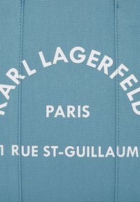 Borsa in tessuto azzurro chiaro con testo bianco audace: "KARL LAGERFELD PARIS 11 RUE ST-GUILLAUME" in un layout arrotondato.