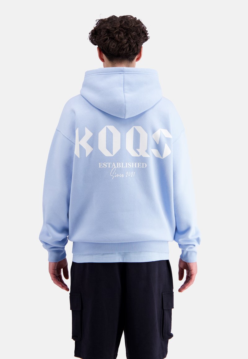 Light blue hooded sweatshirt with white logo "KOQS" and "ESTABLISHED Since 2021" printed on the back. Soft, textured fabric, relaxed fit.