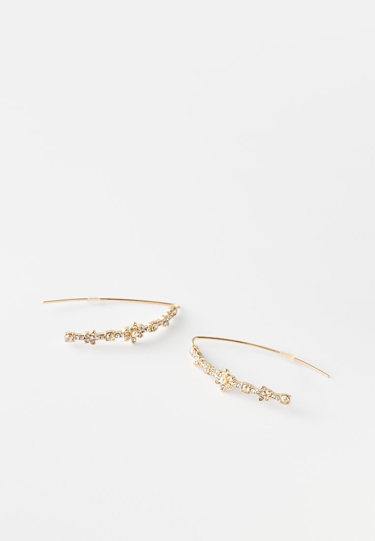 Goldfarbene Ohrringe mit geschwungenem Design, die kleine klare Edelsteine aufweisen, die entlang der Länge in blumigen Mustern angeordnet sind.